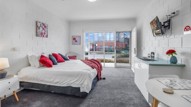 A bedroom with a bed, bedside table, and a view of the outside.