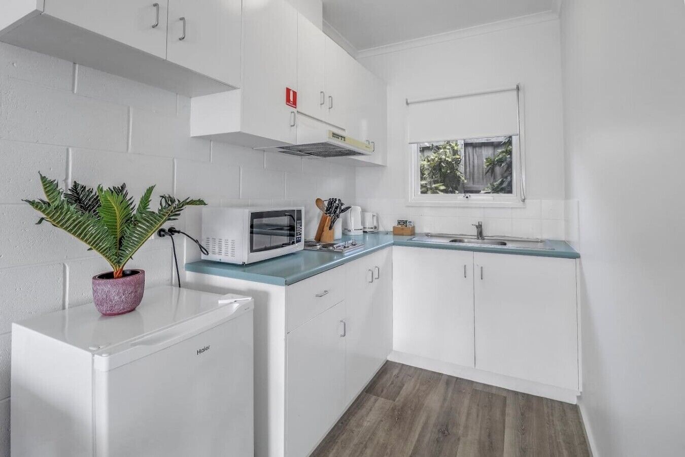 A compact kitchen with white cabinets, a microwave, a sink, and a window.