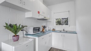 A compact kitchen with white cabinets, a microwave, a sink, and a window.