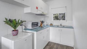 A compact kitchen with white cabinets, a microwave, a sink, and a window.
