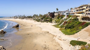 Une plage côtière bordée de propriétés situées en front de mer, notamment des immeubles à plusieurs étages dotés de balcons et offrant une vue dégagée sur l’océan.