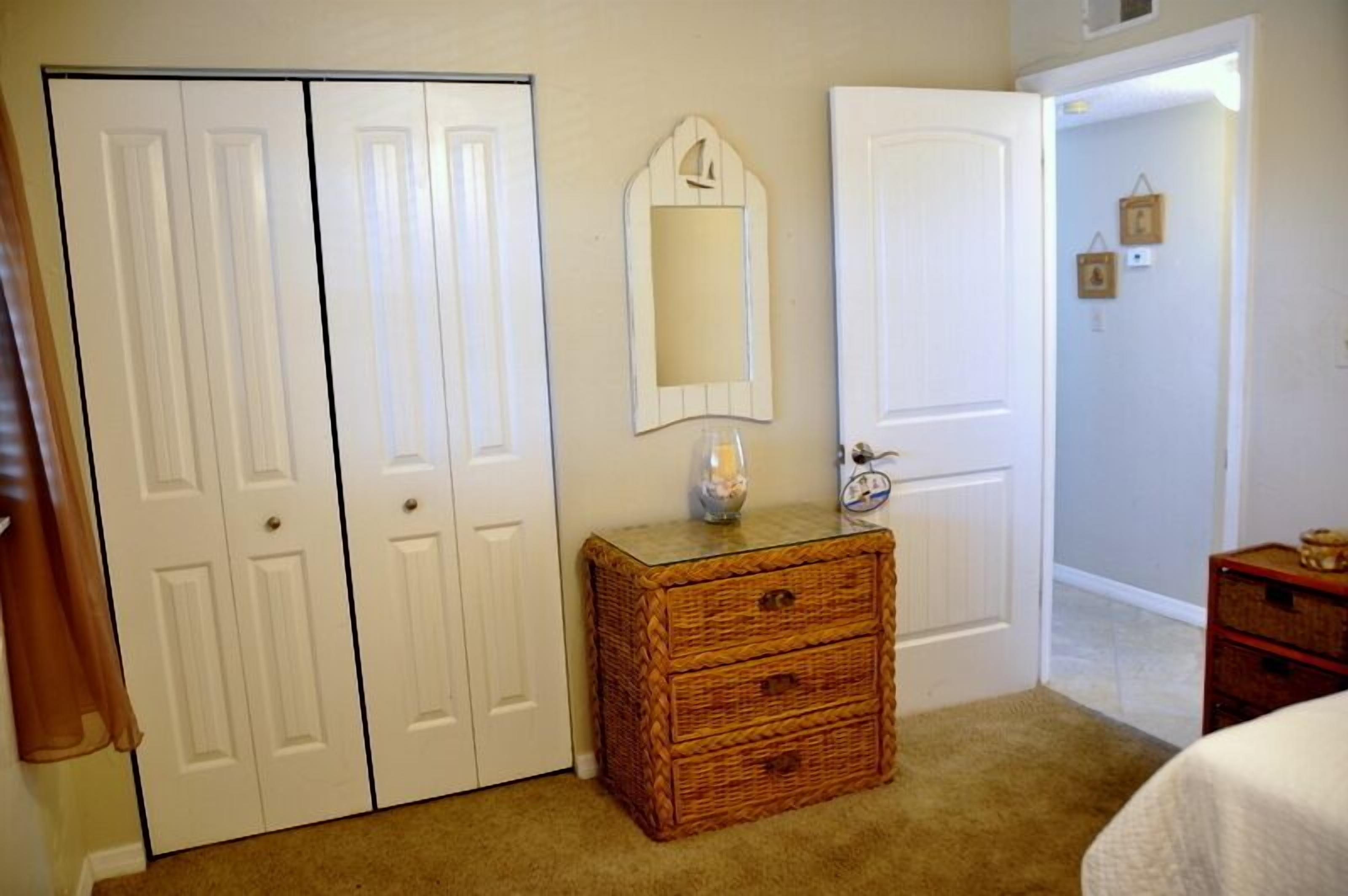 Une chambre avec un placard à deux portes, une petite commode en bois, un miroir et un lit.