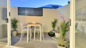 A patio with a table and chairs, surrounded by potted plants and a sliding glass door. - Our flat is a great base to explore everything that South Australia offers... (West Beach)