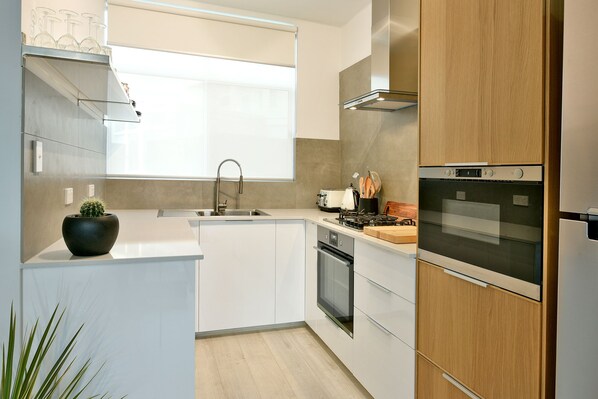 A modern kitchen with white cabinetry, a built-in oven, a stove, and a sink. - Our flat is a great base to explore everything that South Australia offers... (West Beach)