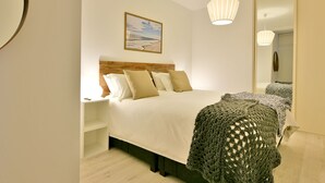A bedroom with a wooden headboard, a large bed, a bedside table, a mirror, and a hanging light fixture. - Our flat is a great base to explore everything that South Australia offers... (West Beach)