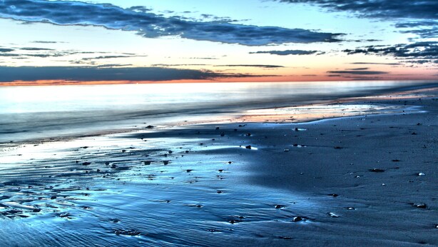 A beach with a smooth, reflective surface and scattered objects. - Our flat is a great base to explore everything that South Australia offers... (West Beach)