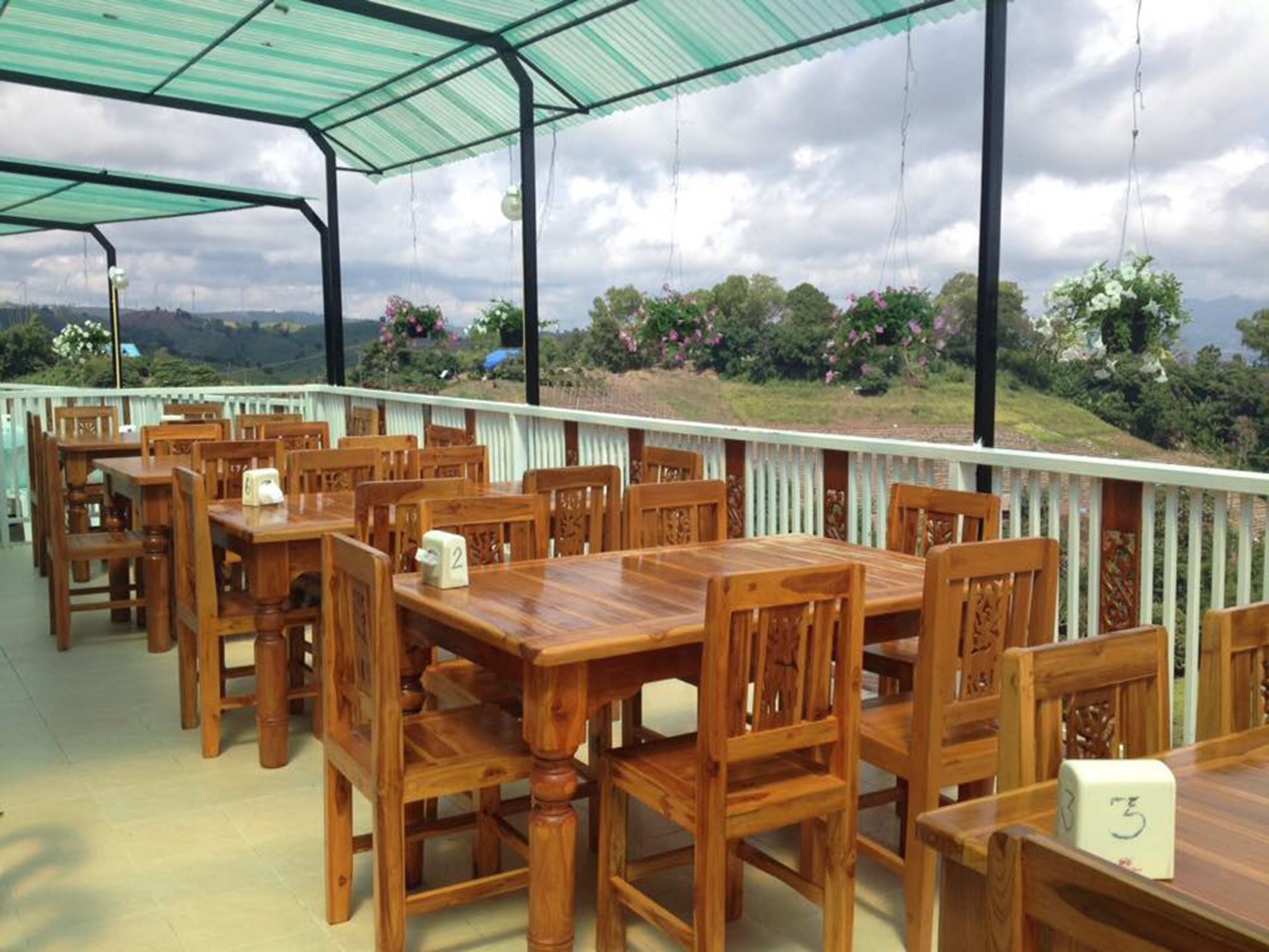 An outdoor dining area with wooden tables and chairs, numbered seating, and a view of the countryside.