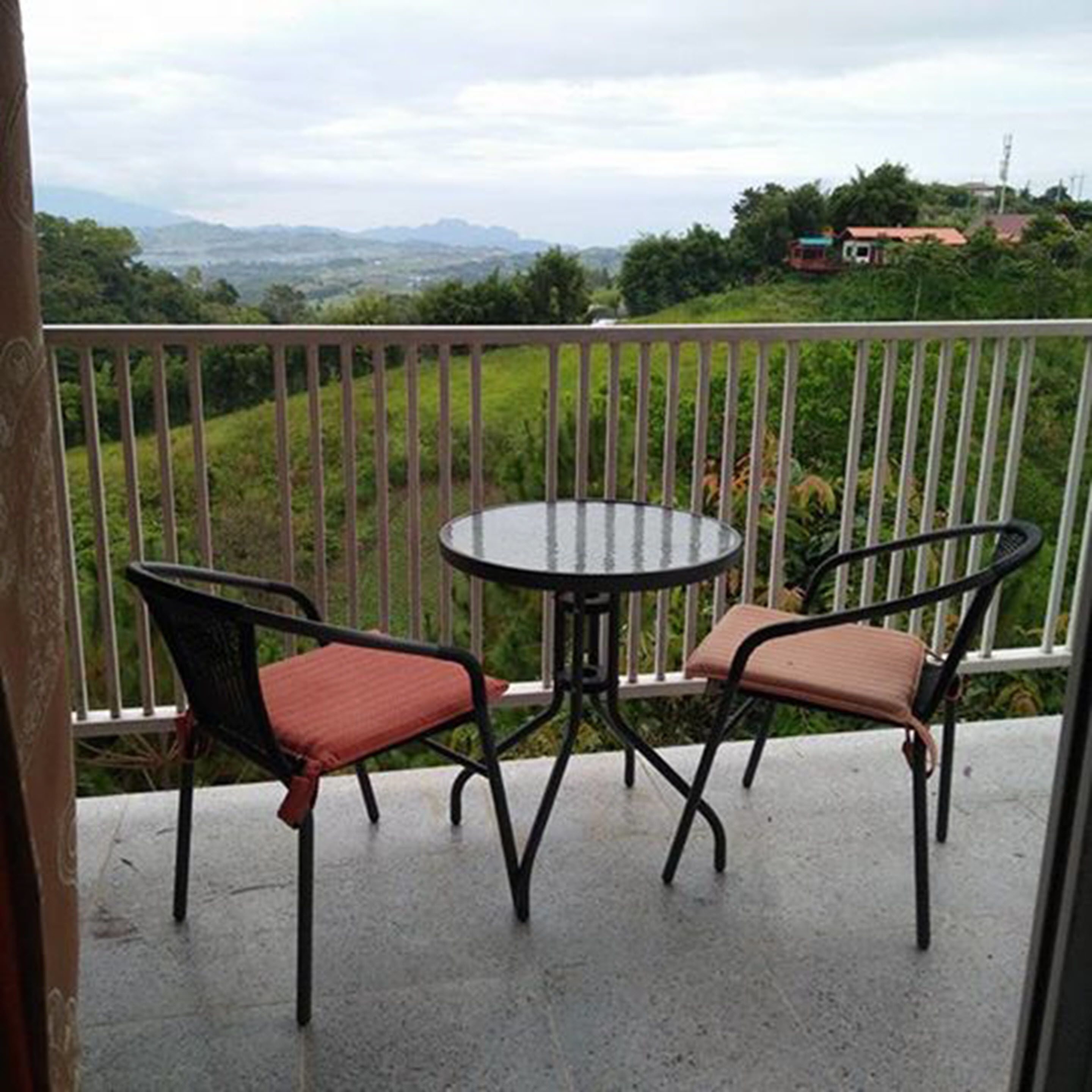 A balcony with two chairs and a table, overlooking a green landscape with distant hills.