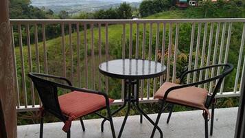 A balcony with two chairs and a table, overlooking a green landscape with distant hills.