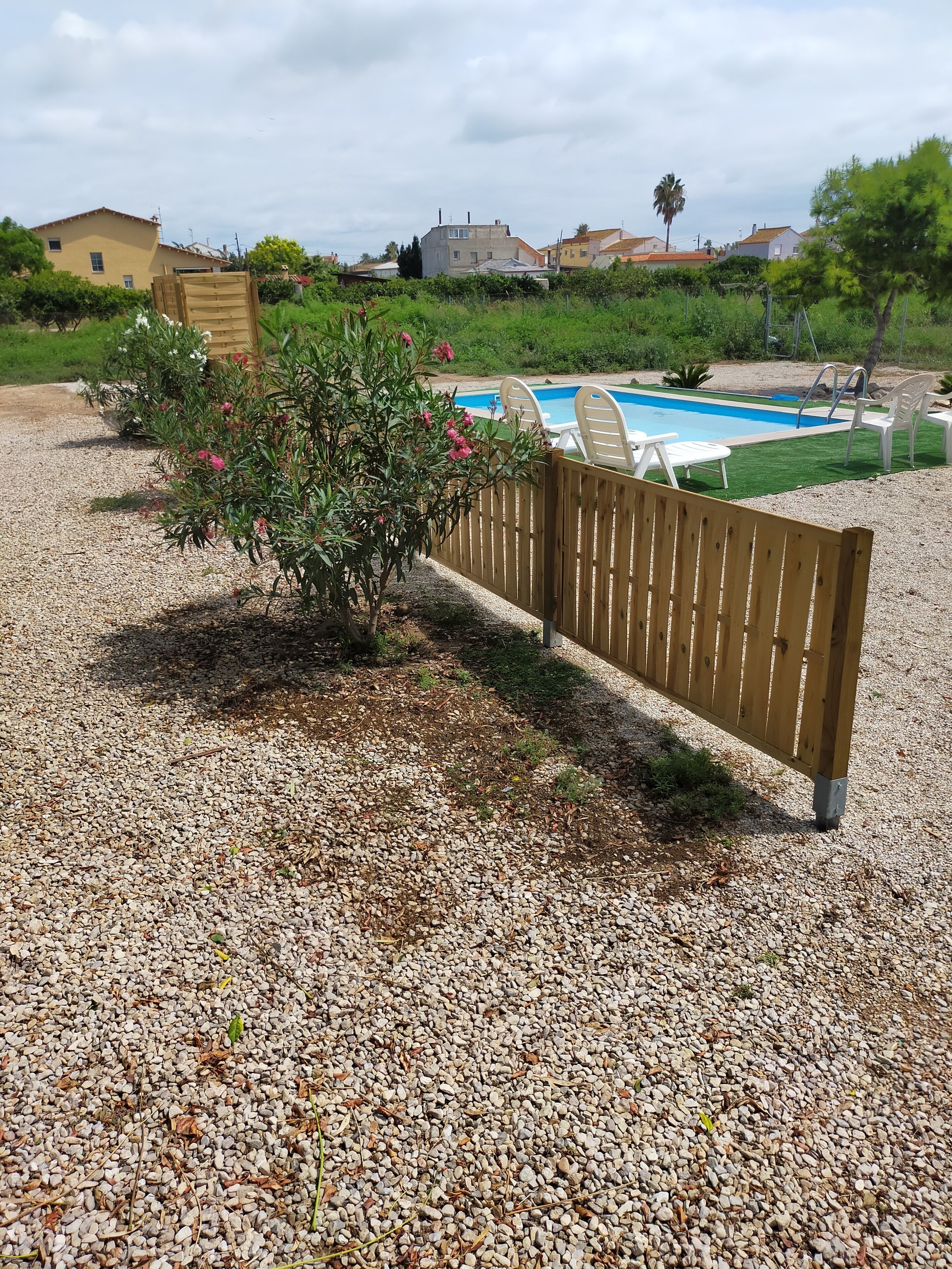 A pool area with a wooden fence, a small bush with pink flowers, and a clear blue pool.