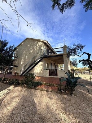 A building with a staircase leading to a covered porch, surrounded by gravel and plants.
