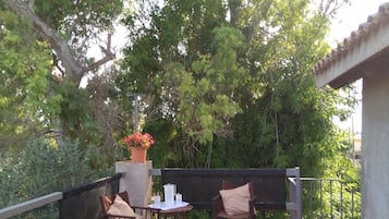 An outdoor patio with a table and two chairs, surrounded by greenery and a railing.
