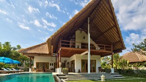 A resort with a pool, a thatched-roof structure, and lush greenery.