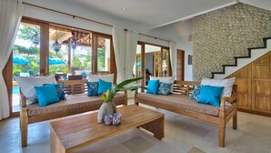 A spacious living area with two wooden sofas, a coffee table, and a staircase with a stone wall.