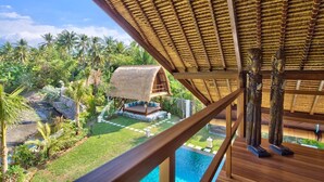 A thatched-roof structure with a pool and lush greenery.