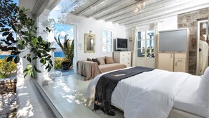 A bedroom with a large bed, a TV, a dresser, and a window overlooking a scenic view. - SEA & SUN A Quality Brand Certified Villa 150 meters from Agia Anna Beach (MYKONOS)