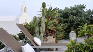 A rooftop lounge with sun loungers, cacti, and a white building with a bell tower in the background. - SEA & SUN A Quality Brand Certified Villa 150 meters from Agia Anna Beach (MYKONOS)