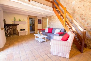 A spacious living area with a sofa, armchair, and a coffee table. A wooden staircase leads to an upper level. - Fantastic chalet with a lot of charm (Algaida)