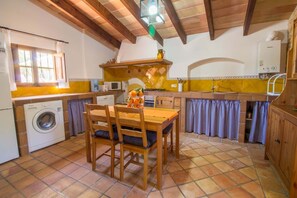 A kitchen with a washing machine, wooden table, chairs, and a tiled floor. - Fantastic chalet with a lot of charm (Algaida)