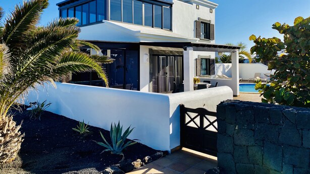 A modern two-story house with a pool, surrounded by tropical plants and a stone wall. - Faro Park, Luxury Villa (VV), heated pool, Sea views,500m shops/bars/restaurants (Playa Blanca)