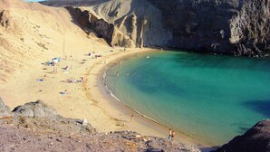 A beach with clear turquoise water, sandy shore, and rocky cliffs. - Faro Park, Luxury Villa (VV), heated pool, Sea views,500m shops/bars/restaurants (Playa Blanca)
