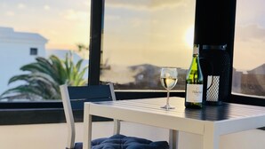 A table with a wine bottle and glass, a chair, and a view of the cityscape through large windows. - Faro Park, Luxury Villa (VV), heated pool, Sea views,500m shops/bars/restaurants (Playa Blanca)