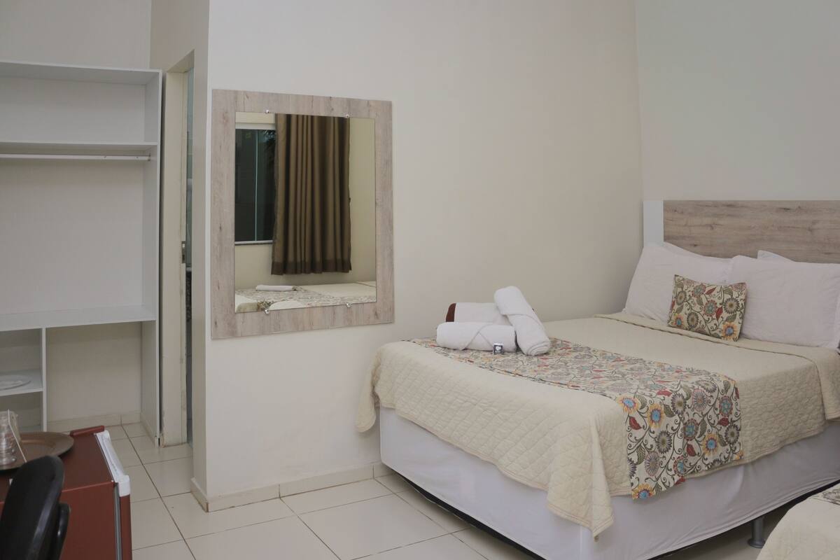 A hotel room with a bed, a desk, a chair, a mirror, and a window with curtains.