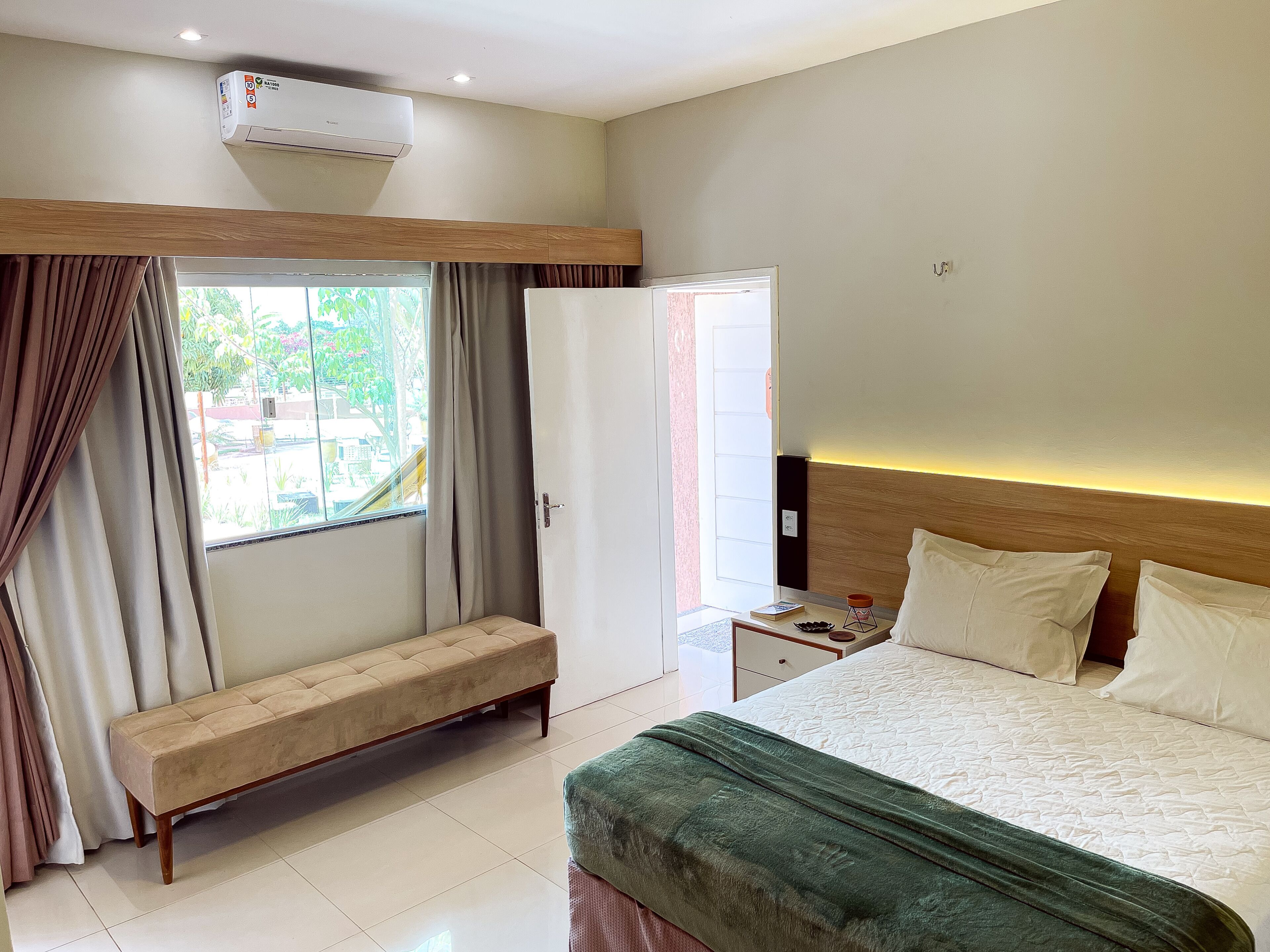 Quarto de hotel com cama, um banco, um guarda-roupa e uma janela com cortinas.