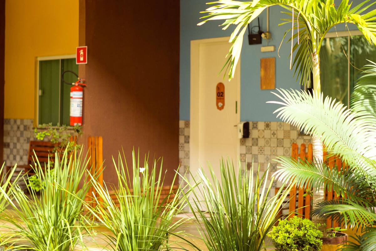 A hotel lobby with a fire extinguisher, a door with a number, and various plants.