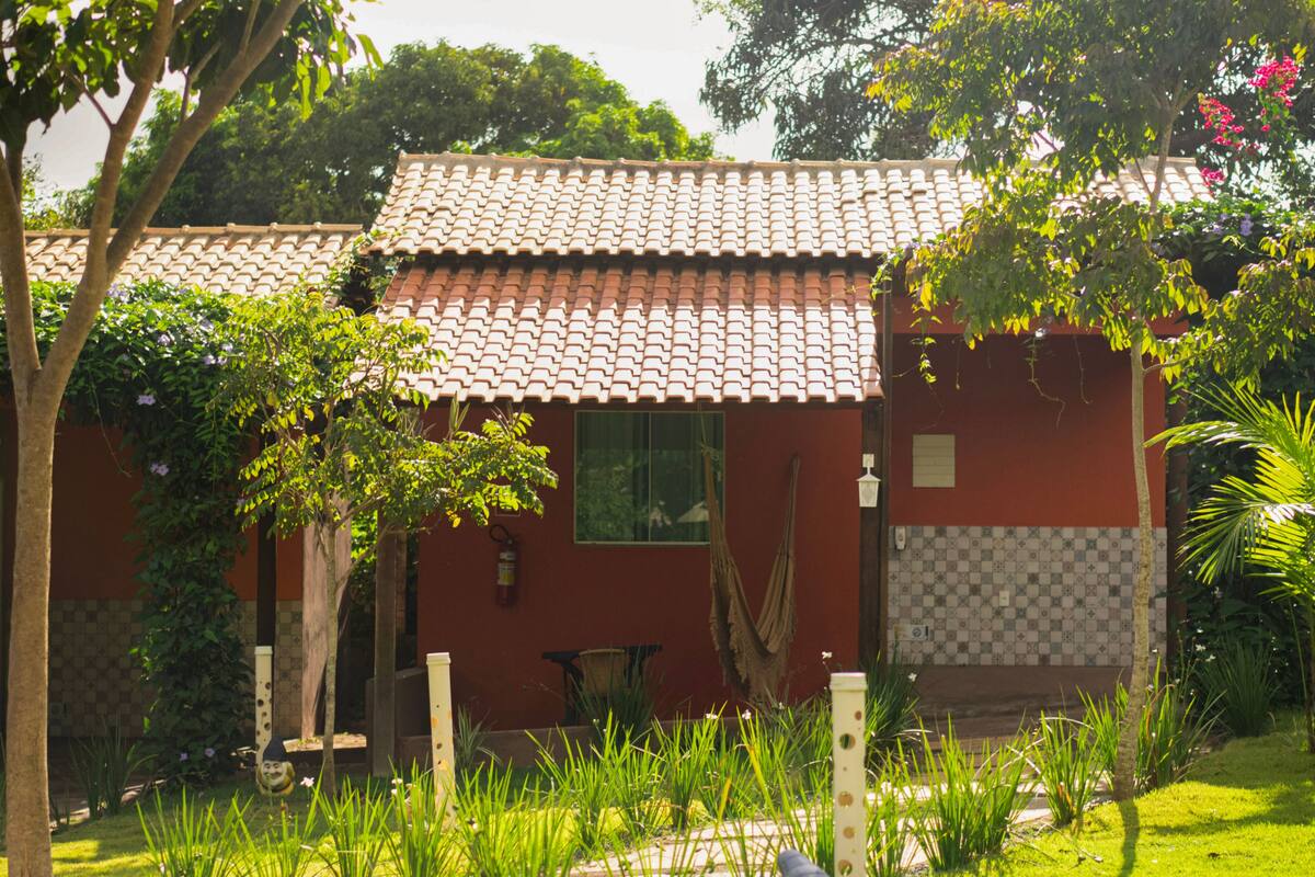 A house with a tiled roof, a small garden with grass and plants, and a hammock hanging on the side.