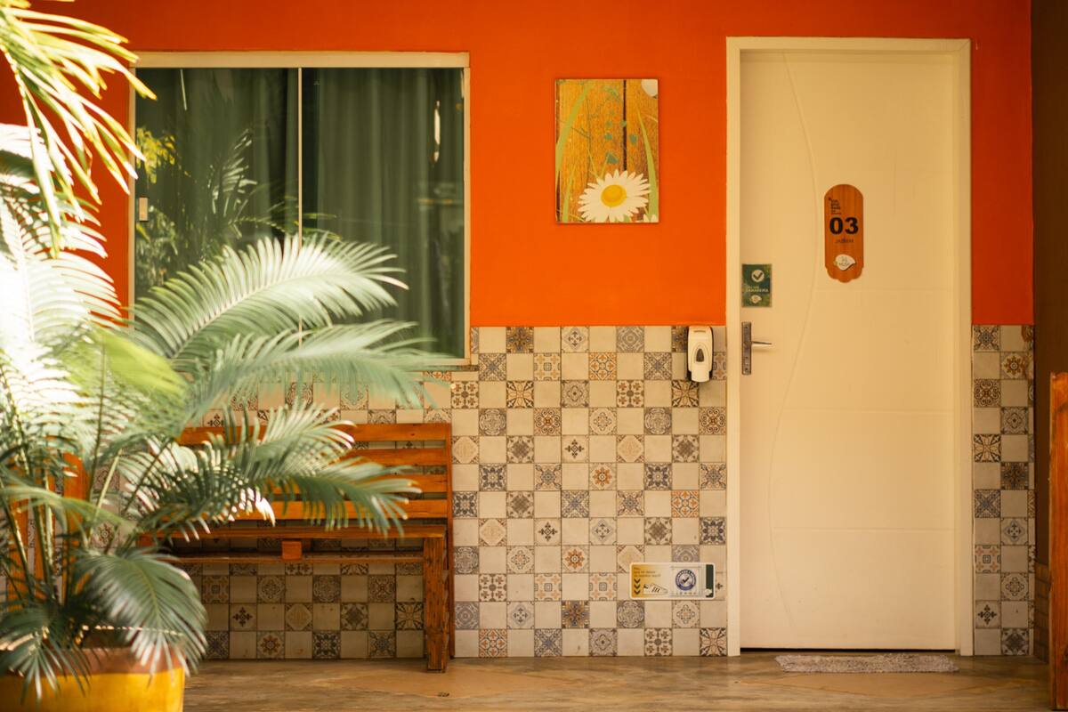 A room with a wooden bench, a potted plant, a door with a number, and a window with curtains.