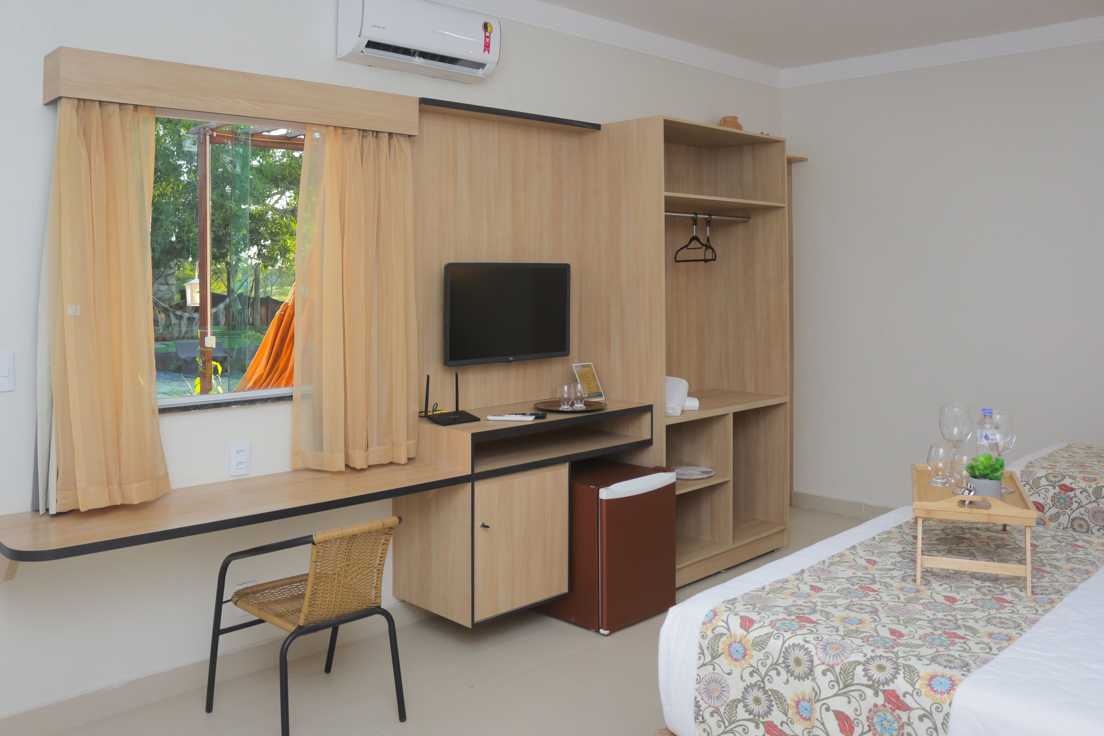 A hotel room with a bed, a desk with a TV, a chair, a wardrobe, and a window with curtains.