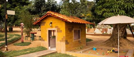 A small yellow building with a tiled roof, surrounded by a garden with a play area.