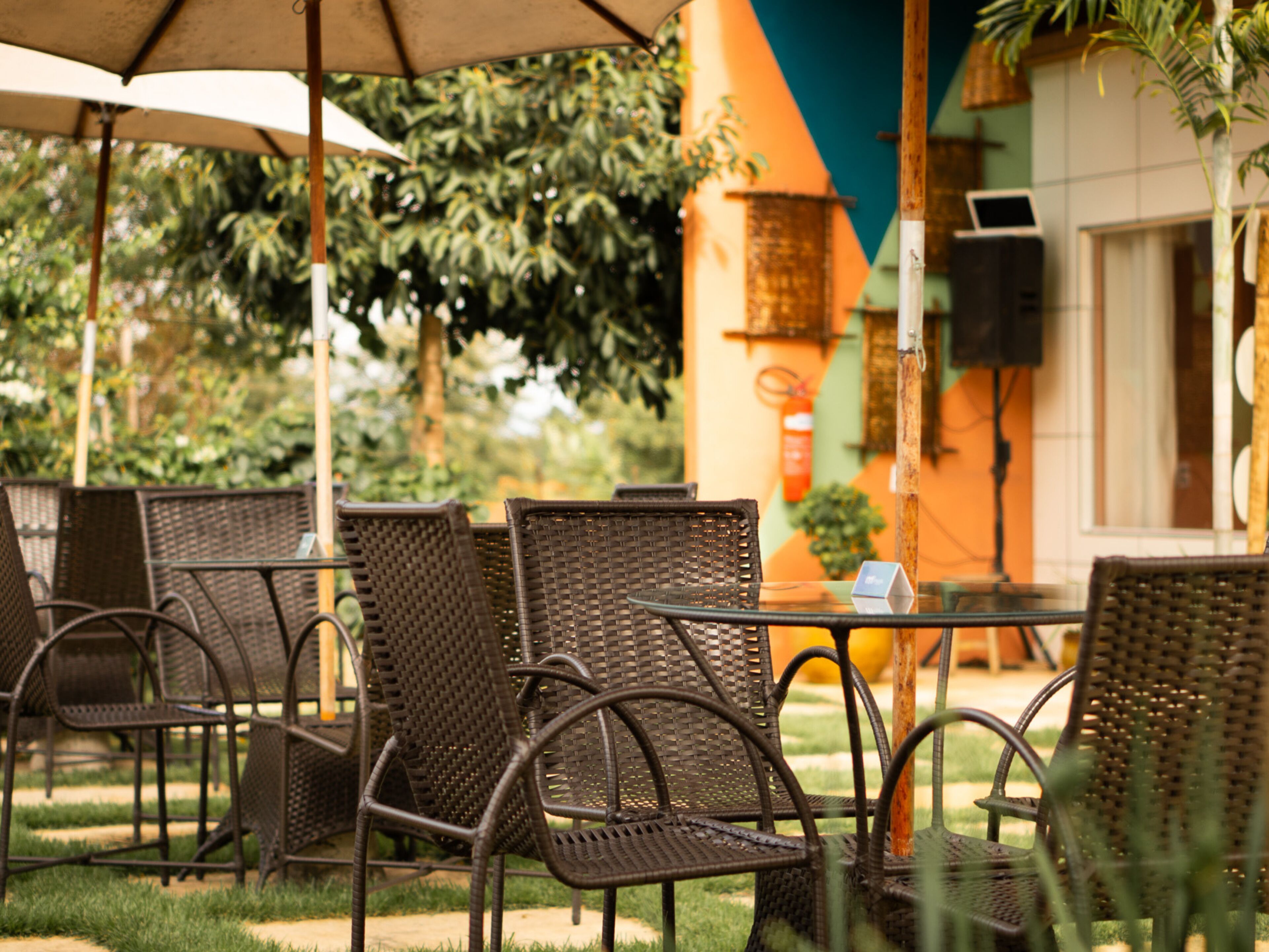 Outdoor wicker furniture with a table and chairs, a fire extinguisher, and a building with a green and orange facade.