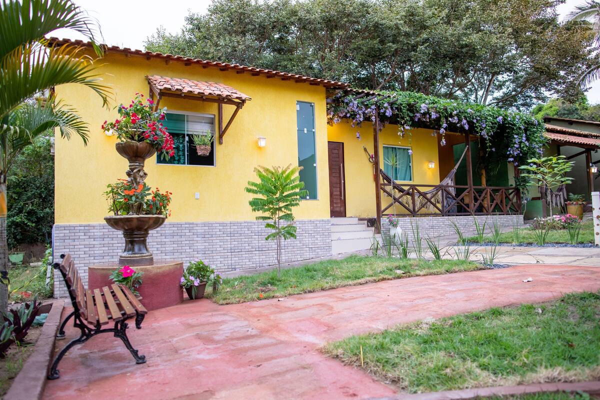 A yellow building with a tiled roof, a bench, a potted plant, and a small garden area.