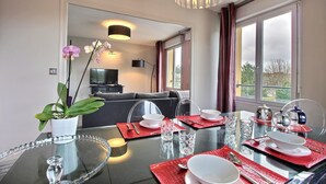 A dining area with a glass table set for four, red placemats, clear glassware, and a potted orchid. - APARTMENT LA COLLINE 4 EPIS - Villas des Sables (Fréhel)