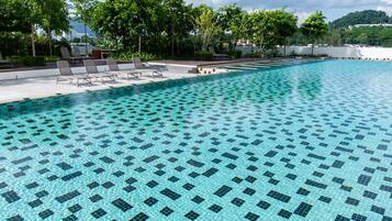 A swimming pool with a tiled pattern, surrounded by lounge chairs and greenery.