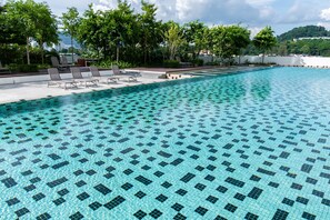 Ein Schwimmbecken mit Kachelmuster, umgeben von Liegestühlen und Grünpflanzen.