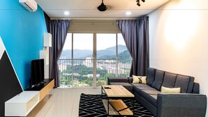 A modern living room with a sofa, coffee table, and TV, a balcony with a city view, and a ceiling fan. - Southwest Designer's Suite by D Imperio Homestay (George Town)