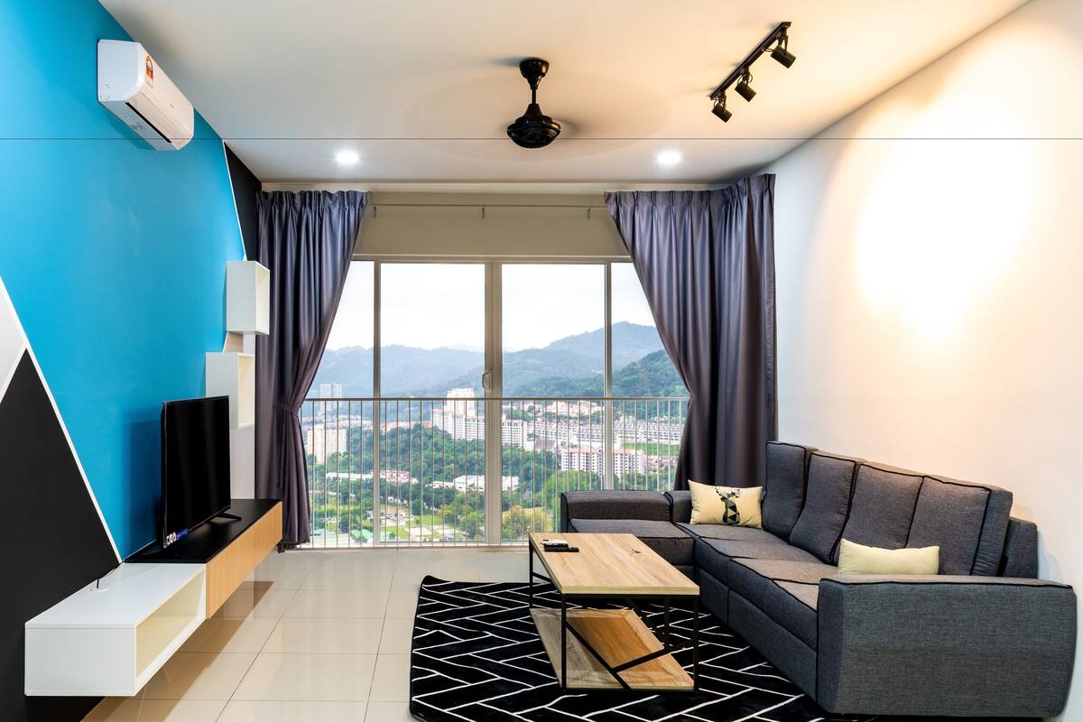 A modern living room with a sofa, coffee table, and TV, a balcony with a city view, and a ceiling fan.