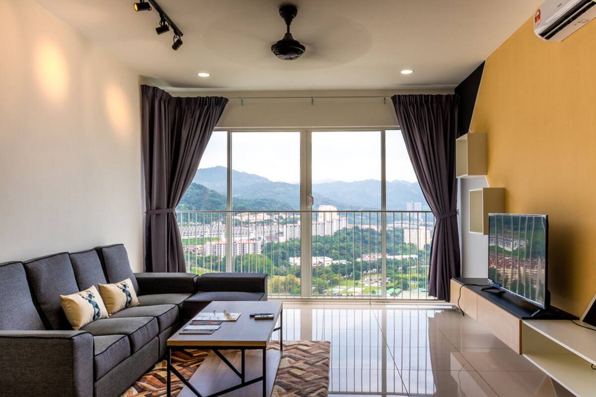 A modern living room with a sofa, coffee table, and TV, large windows with curtains, and a city view.