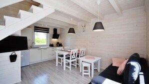 A modern kitchen with white cabinetry, a dining area with white chairs, and a black sofa with a person sitting on it. - The newly built "White Cottage Lux", Grzybowo in Um Kolberg, 1-6 persons (Grzybowo)