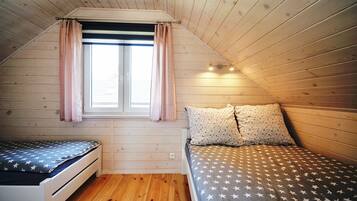 Ein kleiner, gemütlicher Raum mit schrägem Dach, einem fenster mit Vorhängen, einem Bett mit sternenmusternder Bettwäsche und einem kleinen Tisch.