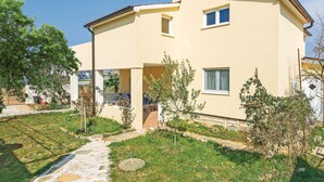 Una casa de dos pisos con techo plano, un pequeño balcón y un jardín con sendero de piedra.