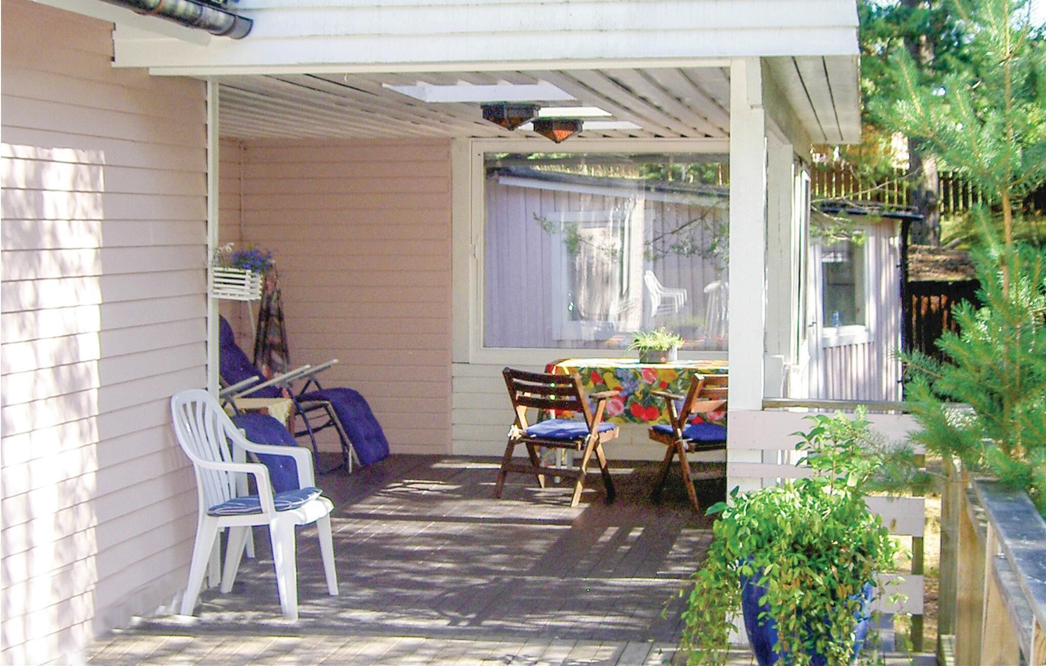 A covered patio with a table and chairs, a white chair, and a potted plant.