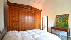A bedroom with a large wooden wardrobe, a bed with white bedding, and a painting on the wall. - Modern renovated holiday home with panoramic terrace, close to sea and mountains (Seneghe)