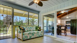 A spacious room with a wooden floor, a sofa with tropical prints, a ceiling fan, and a view of the outdoors. - Large comfy house big enough for 2 families next to ocean on Kaloli point (Keaau)