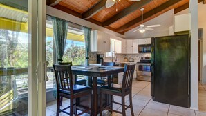 A modern kitchen with white cabinets, a black refrigerator, and a dining area with a wooden table and chairs. - Large comfy house big enough for 2 families next to ocean on Kaloli point (Keaau)