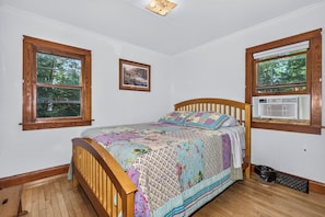 Une chambre à coucher avec un lit en bois, deux fenêtres et un appareil de climatisation.