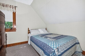A bedroom with a bed, a window with a view of trees, and a wooden dresser. - Gorgeous lakefront cabin, wrap-around enclosed porch, dock! (St Germain)